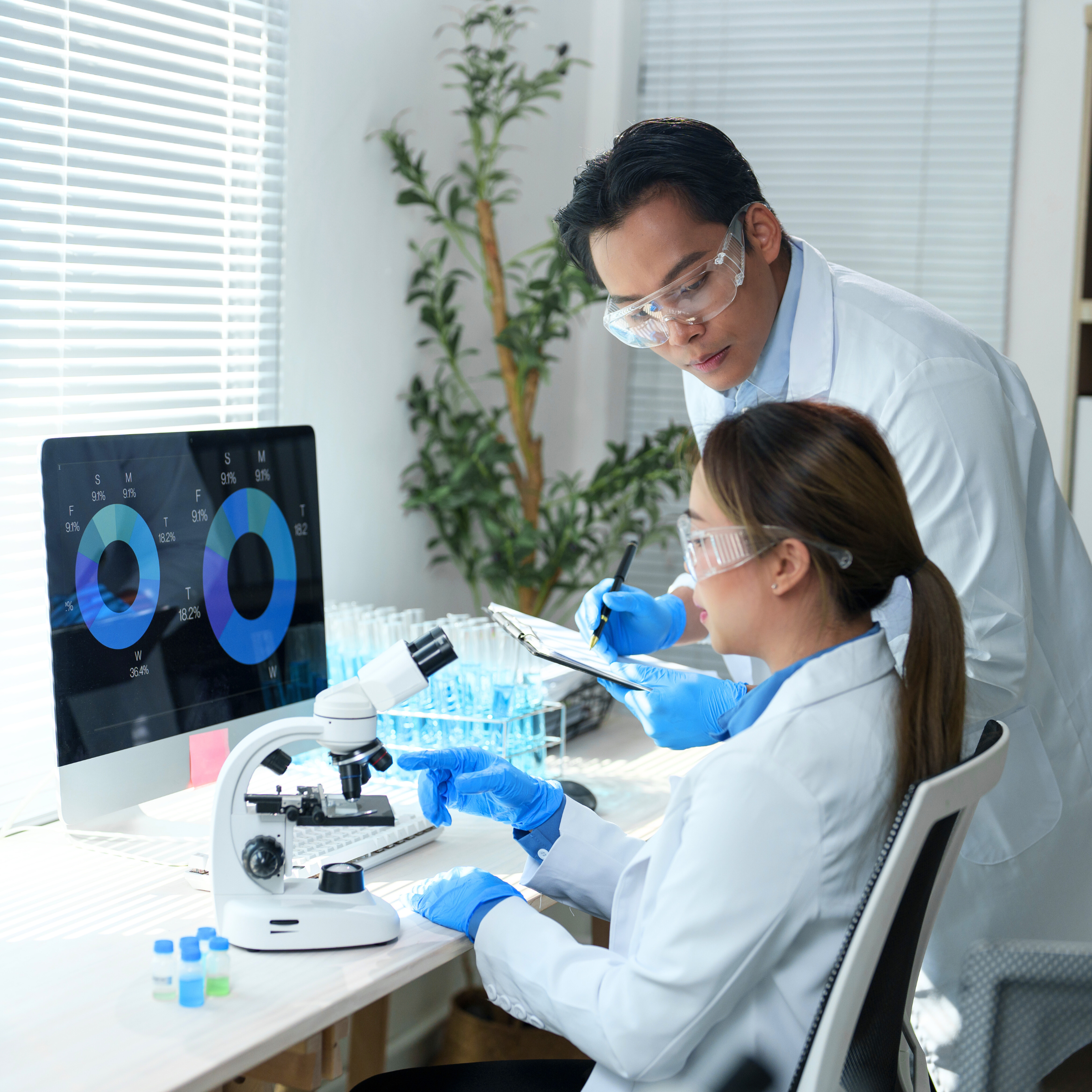 2 research scientist infront of computer and microscope with vials beside it.